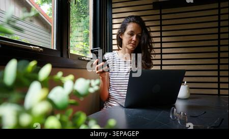 Woman managing multiple communication devices while working at home by a window Stock Photo