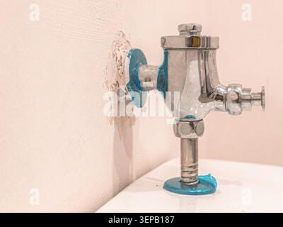 Broken wall beside a chrome flush valve. Blue sealant drips from fittings. Pipe emerges from crumbling plaster. Scene suggests plumbing repair or leakage. Ideal for home maintenance or DIY projects Stock Photo