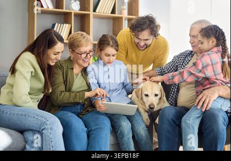 Smiling multigenerational family gathered with pet dog using tablet at home Stock Photo