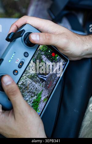 Vertical view of a pilot gripping a drone controller while a small waterfall fills the display. Focus is on controls and tactile details as outdoor fi Stock Photo