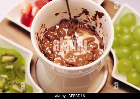 Melted chocolate fondue in ceramic cup with fresh fruit around. Sweet dessert background for dipping snacks party catering and homemade treats. Stock Photo