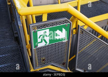 Emergency exit sign on industrial staircase platform. Safety regulations and evacuation route concept in workplace environment. Stock Photo
