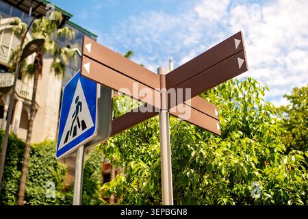 Empty brown directional signposts with white arrows, copy-space, blue pedestrian sign and green trees in background. Stock Photo
