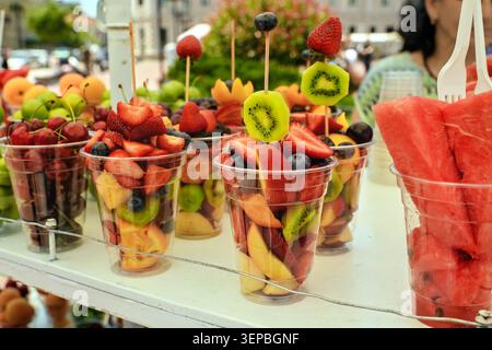Freshly cut fruits, strawberries, cherries and watermelon in plastic takeaway cups on a street food market stall. Stock Photo