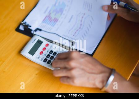 Close-up of hands using a calculator on a financial report with charts, showing budgeting, accounting, tax planning, business analysis, expense tracki Stock Photo