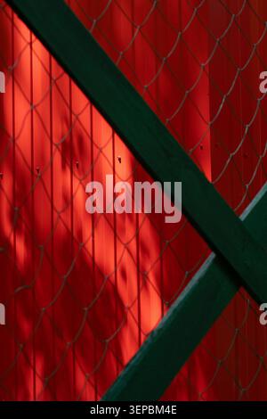 Abstract urban background with bright red metal wall behind a chain-link wire fence and dark wooden beams .  Cinematic aesthetic background featuring Stock Photo