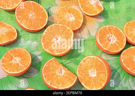 Multiple fresh sliced oranges scattered on a green fabric with floral patterns, showing plump, juicy flesh and vibrant colors, full of fresh summer vi Stock Photo