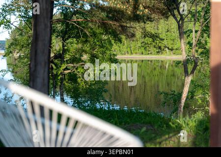 Serene natural landscape with calm water green trees along the shoreline soft reflections on the lake and blurred foreground railing creating depth in Stock Photo