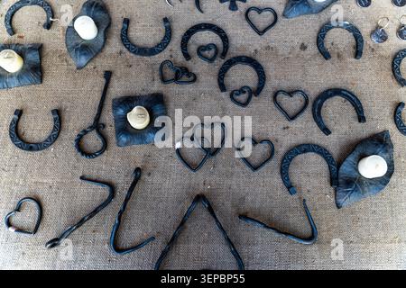 Flat lay of dark metal horseshoes, heart-shaped ornaments small candles arranged on coarse burlap fabric with handmade rustic look soft natural light Stock Photo
