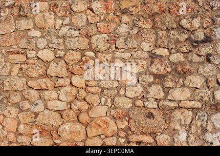 Rough reddish color stone bricks wall, sun shines on Stock Photo