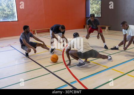 African American men stretching and warming up in athletic gear on hardwood court with orange ball. Basketball, gym, teamwork, camaraderie, practice, Stock Photo