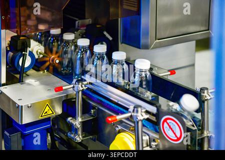 Clear plastic bottles filled with mineral water moving through capping process on production line Stock Photo
