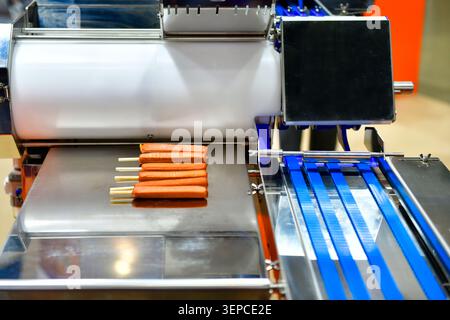 Modern industrial food production machinery manufacturing fresh sausages with wooden sticks in factory Stock Photo