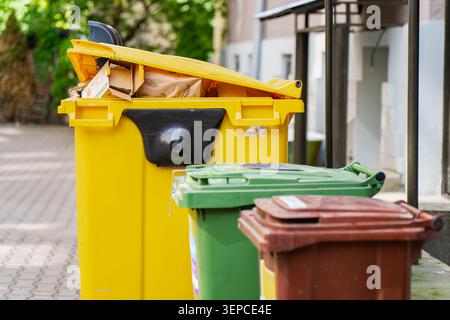 Outdoor waste management system showing selective sorting bins with an overflowing yellow plastic recycling dumpster for residential paper materials Stock Photo