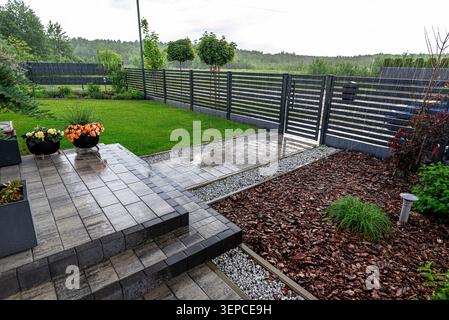 Rain drops falling on paved patio, green lawn, gravel, and bark mulch Stock Photo