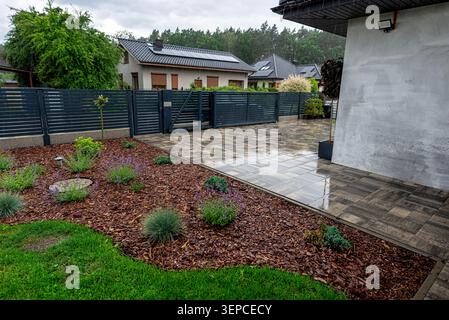 Heavy rain falling on the paved driveway, horizontal slat fence, and green garden Stock Photo