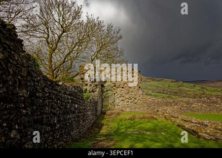 The ruins of a castle wall are in sunshine as black clouds of a hailstorm sweep in across a wide valley, Peveril Castle, Castleton, Peak District. Stock Photo