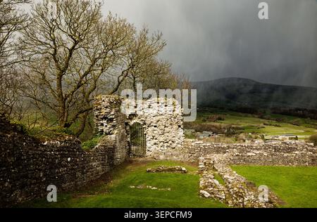 The ruins of a castle wall are in sunshine as black clouds of a hailstorm sweep in across a wide valley, Peveril Castle, Castleton, Peak District. Stock Photo