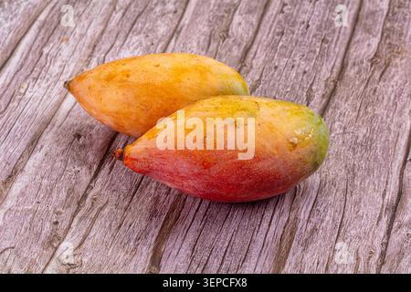 Two ripe mangoes with orange, red, and green hues resting on weathered wooden planks, showcasing fresh tropical fruit Stock Photo