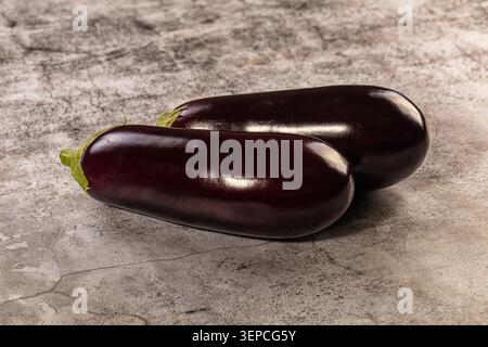 Two ripe shiny eggplants with green stems lying on textured gray surface, perfect for vegetarian cuisine and healthy lifestyle concepts Stock Photo