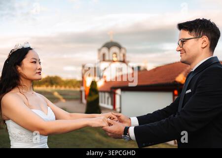 Interracial wedding couple holding hands in front of church Stock Photo