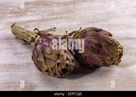 Two fresh raw globe artichokes displayed on textured light white wooden background. Healthy organic vegetable, still life food photography. Natural li Stock Photo