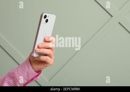 Womans hand holding modern smartphone for digital communication and mobile technology on green background, the device is used for internet connectivit Stock Photo