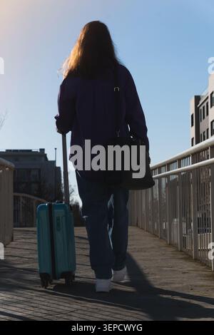 Woman pulling a light blue suitcase moving forward on a sunny day Stock Photo