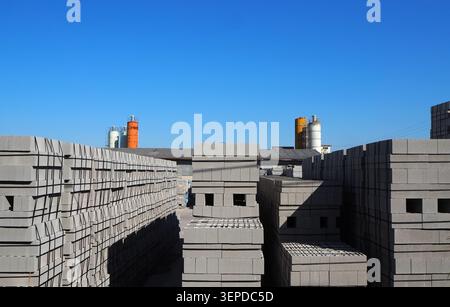 Cement blocks stacked outside the precast concrete factory. Silos on background Stock Photo