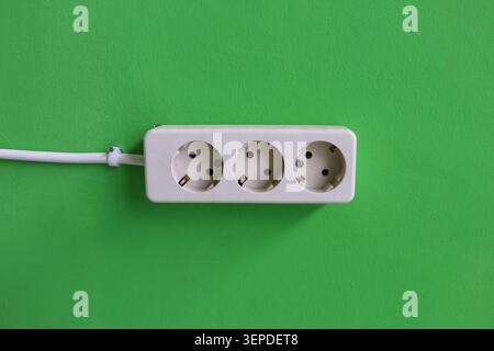White Triple Electrical Power Outlet on Green Wall Background with Copy Space, Household Electricity Socket Installation and Energy Connection Concept Stock Photo