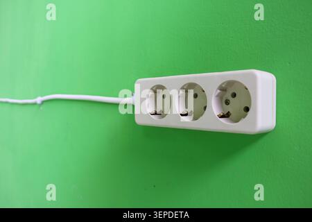 White Triple Electrical Power Outlet on Green Wall Background with Copy Space, Household Electricity Socket Installation and Energy Connection Concept Stock Photo