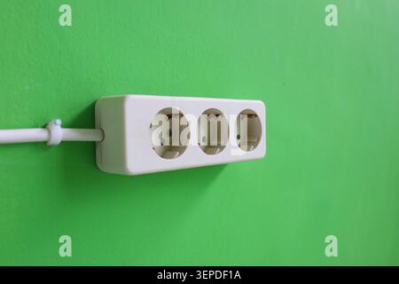 White Triple Electrical Power Outlet on Green Wall Background with Copy Space, Household Electricity Socket Installation and Energy Connection Concept Stock Photo