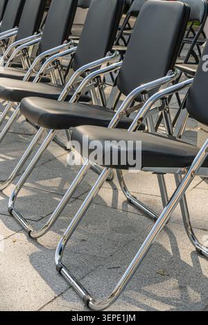 Black folding chairs are neatly arranged in rows at an outdoor venue, creating a strong geometric pattern suitable for event and organization concepts Stock Photo
