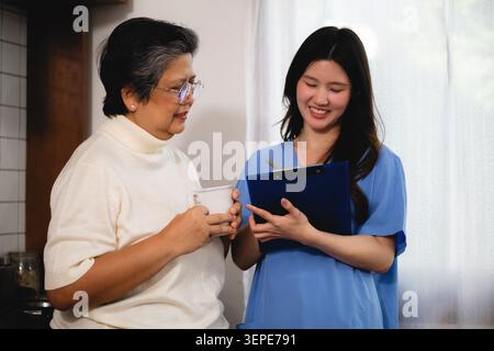 Smiling asian nurse showing medical checklist senior woman, consulting mature asian senior woman holding mug, discussing test results older patient Stock Photo