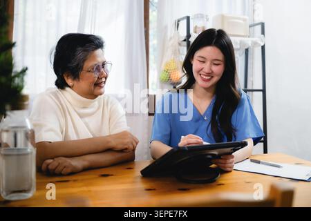 Smiling asian nurse showing digital tablet senior woman, explaining medical data older patient, consulting elderly lady digital tablet, discussing hea Stock Photo