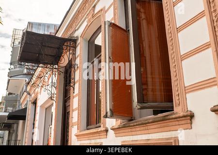 An architectural detail of an old European-style building facade with open wooden frame windows, jalousie, and an ornate metal awning. Stock Photo