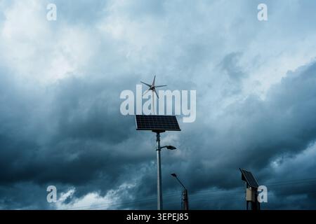 A modern off-grid street lamp equipped with a small wind turbine and a solar panel, standing against a dark, dramatic background of heavy storm clouds Stock Photo