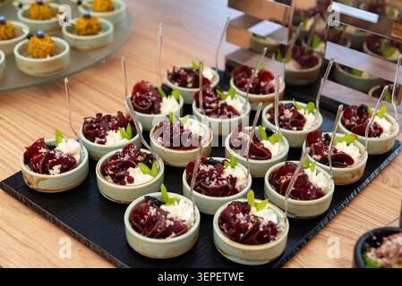 Small ceramic cups filled with whipped cream and colorful jellied fruit served with clear plastic spoons on table. Stock Photo