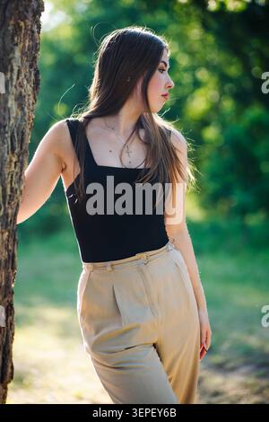Thoughtful young woman leaning against a tree in a park, enjoying the peaceful atmosphere and fresh air Stock Photo