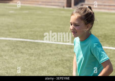 Female child standing on sports turf near white boundary in teal T-shirt looking right, copy space Stock Photo