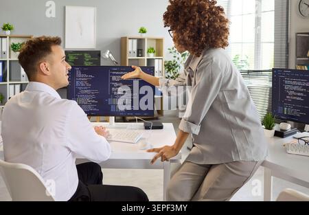 Software developers collaborating in office, reviewing code on dual monitors Stock Photo