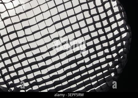 Close-up texture of a black honeycomb grid on a professional photography studio softbox with white light shining through, creating a dark abstract geo Stock Photo