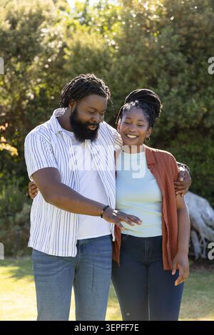 Couple standing on grassy lawn, man in striped shirt pointing while woman in rust shirt smiling Stock Photo