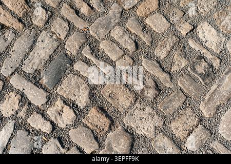 Close-up of irregular historic cobblestone pavement with rough stones, gravel filling, natural outdoor light, and detailed old street surface texture. Stock Photo