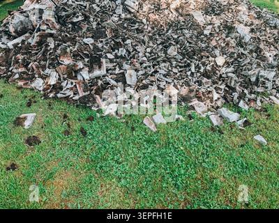 Large pile of construction and demolition debris scattered on a grassy area. Detailed texture of broken masonry and building materials, ideal for wast Stock Photo