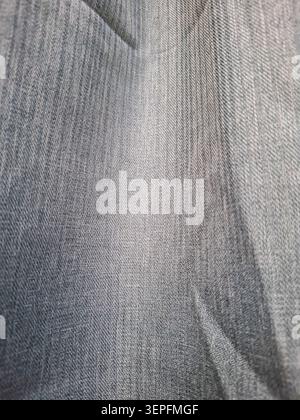 The scene shows a close-up of grey or denim-like fabric texture. Soft light reflects off the surface, highlighting the fine woven patterns that can in Stock Photo