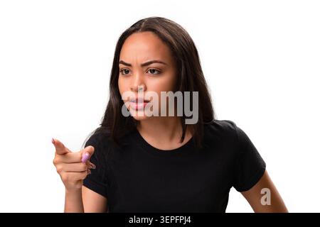 Furious and upset young Hispanic woman looking aside with an angry facial expression and pointing her finger. Studio shot representing conflict, blame Stock Photo