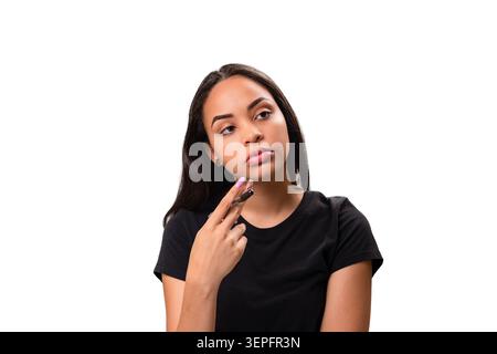 Thoughtful and curious young Hispanic woman holding her hand on her chin, looking up and aside. Studio shot representing decision making, brainstormin Stock Photo