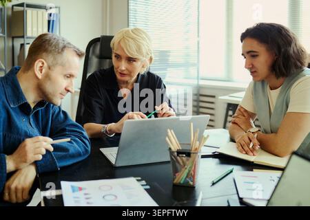 Diverse business team reviewing laptop data, discussing strategy, collaborating during office meeting. Ideal for workplace teamwork, project planning, leadership, corporate marketing Stock Photo