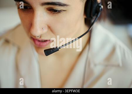 Close up face of young Hispanic woman wearing headset, assisting customers in call center office and handling support communication. Ideal for customer service, help desk, CRM Stock Photo